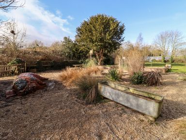 An outdoor garden area with gravel ground a large tree various plants a picnic table and a sculpture of a pig at Wick Court Farm in Arlingham near Frampton On Severn