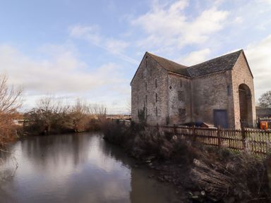 A river beside an old brick barn with a wooden fence near Wick Court Farm in Arlingham near Frampton On Severn