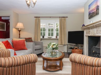 A living room with striped armchairs a glass top wooden coffee table a grey sofa and a TV near a fireplace at Early Mist Cottage in Haytor Vale