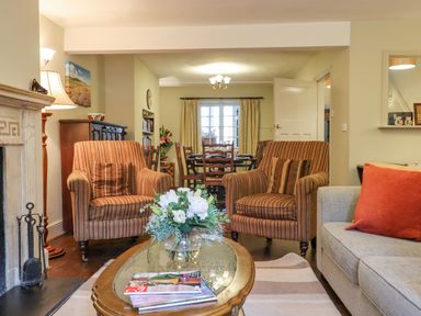 A living room with armchairs a coffee table a bouquet of flowers and a dining area in the background at Early Mist Cottage in Haytor Vale