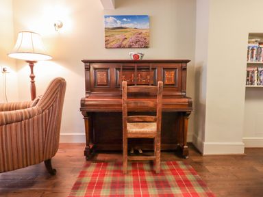 A wooden piano with a wooden chair in front and a lamp next to a striped armchair at Early Mist Cottage in Haytor Vale