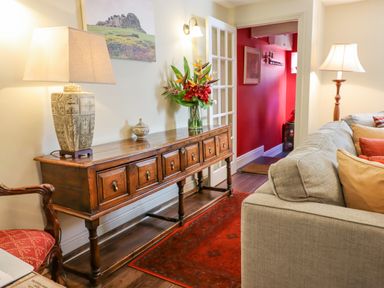 A living room with a wooden sideboard holding a lamp and flowers next to a beige sofa at Early Mist Cottage in Haytor Vale
