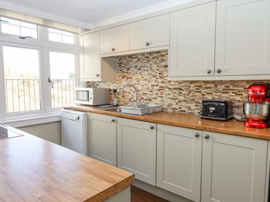 A kitchen with light-colored cabinets wooden countertops a microwave a dishwasher a toaster a red stand mixer and a window at Early Mist Cottage in Haytor Vale