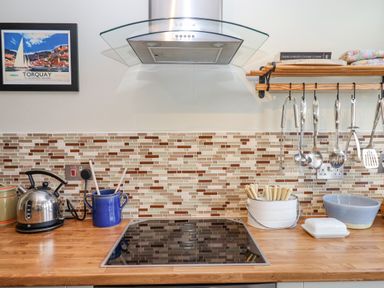 A kitchen countertop with an electric kettle blue utensil holder and cooking utensils hanging at Early Mist Cottage in Haytor Vale