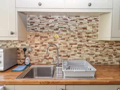 A kitchen sink with a silver faucet and dish rack on a wooden countertop with mosaic tile backsplash at Early Mist Cottage in Haytor Vale