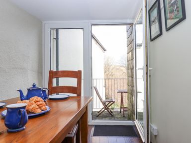 A dining area with a wooden table and chairs blue teapot and croissants on the table and an open door leading to a small balcony with a folding chair and table at Early Mist Cottage in Haytor Vale