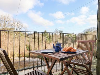 A balcony with a wooden table and chairs with a teapot and croissants overlooking trees at Early Mist Cottage in Haytor Vale