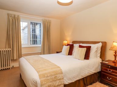 A bedroom with a double bed, bedside tables with lamps, a window with curtains, and a radiator at Early Mist Cottage in Haytor Vale