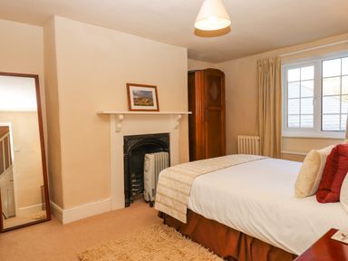A bedroom with a bed near a window a mirror leaning against the wall and a small fireplace at Early Mist Cottage in Haytor Vale