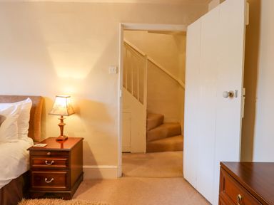 A bedroom with a bedside table lamp next to a bed and an open door showing stairs at Early Mist Cottage in Haytor Vale