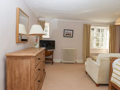 A room with a wooden dresser lamp flat screen tv armchair windows and radiator at Early Mist Cottage in Haytor Vale