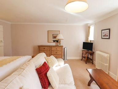 A sitting area with a beige couch and cushions beside a wooden chest of drawers with a lamp and mirror above at Early Mist Cottage in Haytor Vale