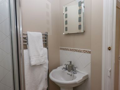 A bathroom with a white pedestal sink a wall-mounted mirror and towels on a heated rail at Early Mist Cottage in Haytor Vale