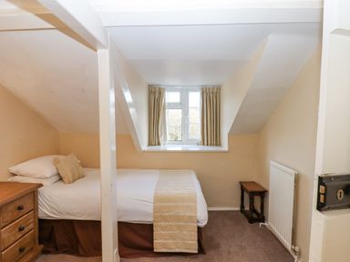 A small bedroom with a single bed beside a wooden dresser and a window with curtains at Early Mist Cottage in Haytor Vale