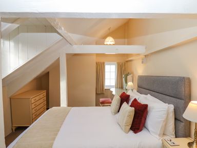 A bedroom with a bed with pillows bedside tables lamps a chest of drawers and a window with curtains at Early Mist Cottage in Haytor Vale