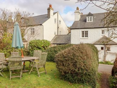 A garden area with wooden table and chairs and a blue umbrella near white houses at Early Mist Cottage in Haytor Vale