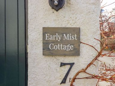 A stone wall with a sign reading Early Mist Cottage and the number 7 with a dark green door and a branch at Early Mist Cottage in Haytor Vale