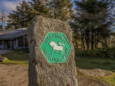 A stone marker with a dartmoor national park sign surrounded by trees and a building in the background at Early Mist Cottage in Haytor Vale