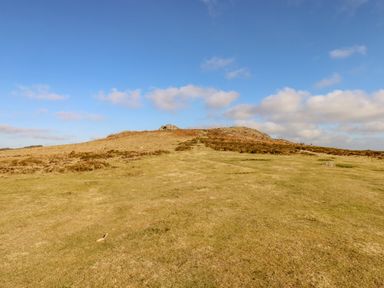 A grassy hill with rocky outcrops under a blue sky with scattered clouds at Early Mist Cottage in Haytor Vale