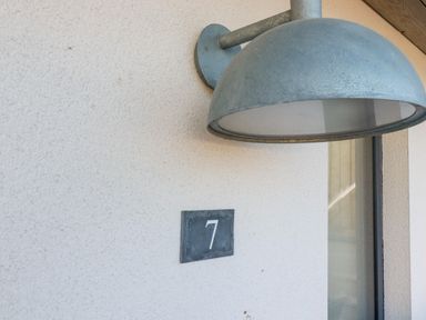 A metal light fixture above a number 7 wall plaque on an exterior wall at 7 Longshore in St Columb Minor