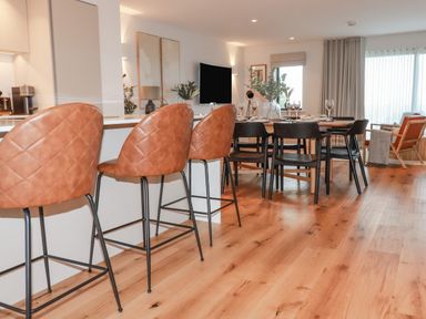 A dining area with brown bar stools at a kitchen counter and a wooden dining table with black chairs at 7 Longshore in St Columb Minor