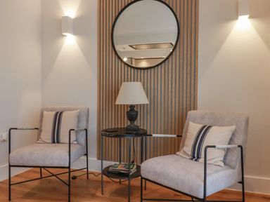 A sitting area with two upholstered chairs a small round table with a lamp and a round mirror on a wooden panel at 7 Longshore in St Columb Minor