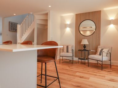 A sitting area with two chairs a round mirror and a small table with a lamp next to a kitchen island at 7 Longshore in St Columb Minor