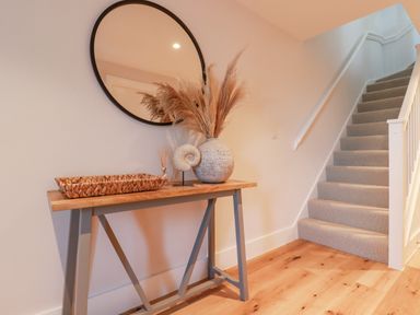 A hallway with a wooden table and a round mirror above next to carpeted stairs at 7 Longshore in St Columb Minor