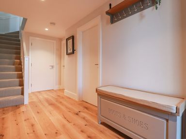 A hallway with wooden floor a carpeted staircase white doors a bench with Boots and Shoes written on it and a wall-mounted coat rack at 7 Longshore in St Columb Minor