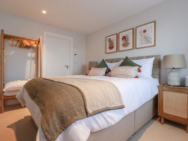 A bedroom with a bed a bedside table a lamp three framed artworks and a wooden clothes rack at 7 Longshore in St Columb Minor