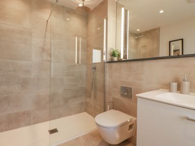 A bathroom with a walk in shower a wall mounted toilet and a sink with soap dispensers at 7 Longshore in St Columb Minor