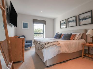 A bedroom with a bed pillows a striped blanket a wooden chair a wall mounted TV and framed pictures at 7 Longshore in St Columb Minor