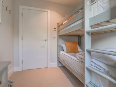 A bedroom with a bunk bed a white door and a small cabinet at 7 Longshore in St Columb Minor