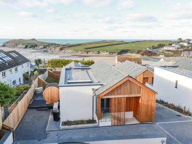 A modern house with wooden exterior elements near a beach and grassy hills at 7 Longshore in St Columb Minor