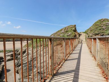 A wooden bridge with metal railings leading to a path between grassy hills at 7 Longshore in St Columb Minor