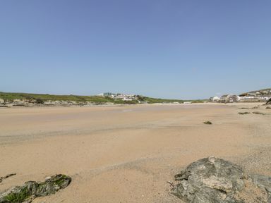 A sandy beach with rocks in the foreground and buildings in the distance at 7 Longshore in St Columb Minor