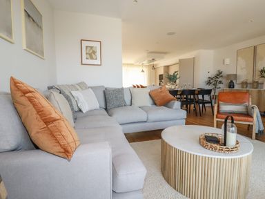 A living room with a gray sectional sofa orange pillows and a round wooden coffee table at 7 Longshore in St Columb Minor