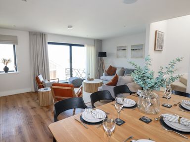 A dining and living area with a set dining table and seating with sliding glass doors at 7 Longshore in St Columb Minor