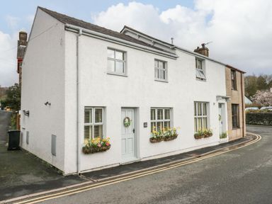 A white two-story house with flower boxes under the windows and gray doors on a curved street at The Anvil in Broughton-In-Furness