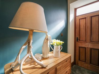 A wooden sideboard with a lamp with antler base vase with flowers and ceramic rabbit figurine near a wooden door at The Anvil in Broughton-In-Furness