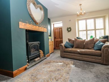 A living room with a brown sofa pillows a fireplace with a heart mirror and string lights and a rug on the floor at The Anvil in Broughton-In-Furness