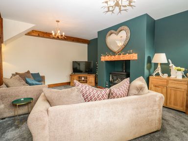 A living room with beige sofas a TV on a wooden stand a fireplace with a heart shaped mirror and fairy lights at The Anvil in Broughton-In-Furness