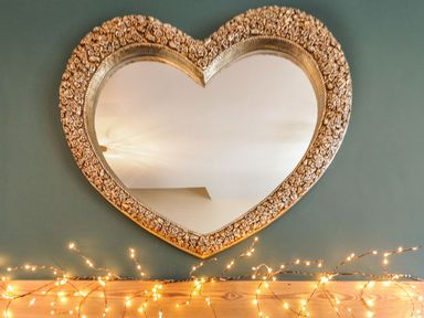 A heart shaped decorative mirror on a green wall with string lights below it at The Anvil in Broughton-In-Furness