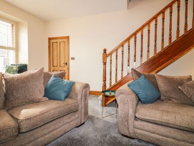 A living room with two brown sofas and blue cushions near a wooden staircase and a wooden door at The Anvil in Broughton-In-Furness