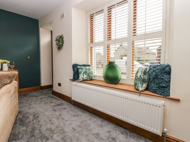 A room with a window seat decorated with cushions and a green vase above a radiator