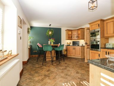 A kitchen with wooden cabinets green bar stools and a small dining table at The Anvil in Broughton-In-Furness