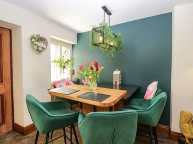 A dining area with green chairs around a wooden table and a vase with red tulips at The Anvil in Broughton-In-Furness