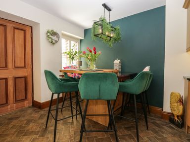 A dining area with green chairs around a wooden table and flowers on the table at The Anvil in Broughton-In-Furness
