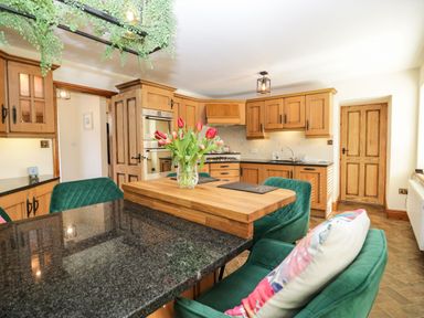 A kitchen with wooden cabinets a black countertop a wooden island with a vase of flowers and green chairs at The Anvil in Broughton-In-Furness