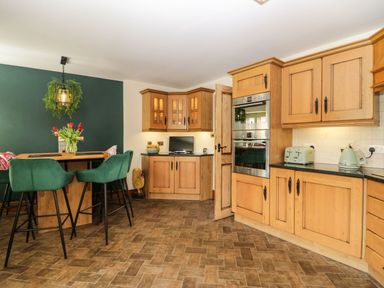 A kitchen with wooden cabinets green chairs a wooden island and a dining area at The Anvil in Broughton-In-Furness